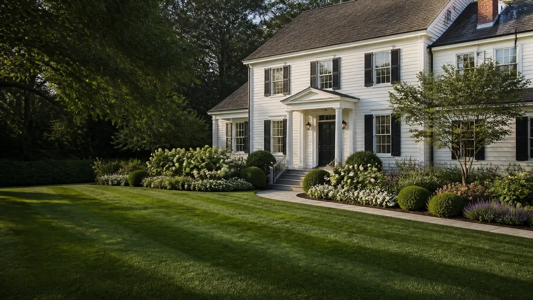 New England colonial home framed by layered gardens and a freshly striped lawn